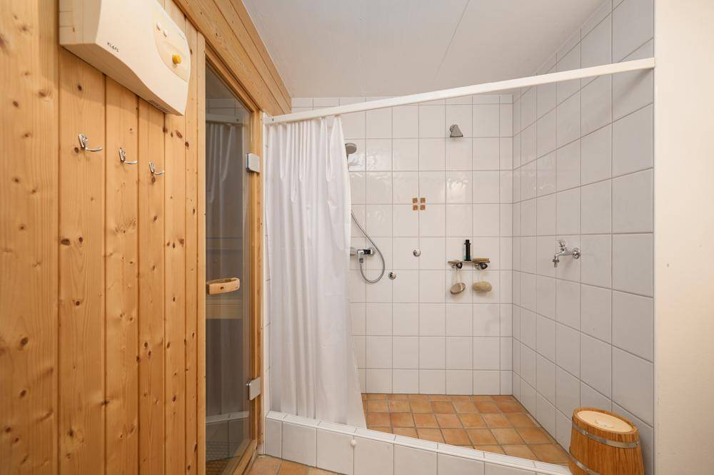 Badezimmer mit Duschbereich und integrierter Sauna, ausgestattet mit Holzverkleidung und Fliesen.