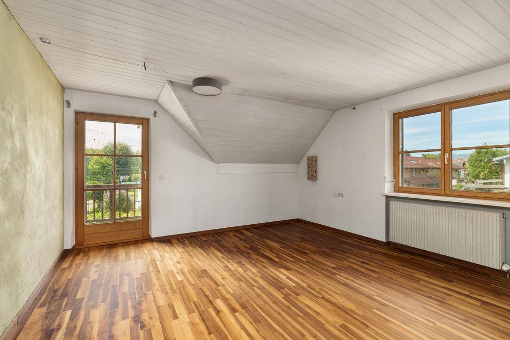 Geräumiges Schlafzimmer mit Holzboden, Dachschräge und Zugang zu einem kleinen Balkon.