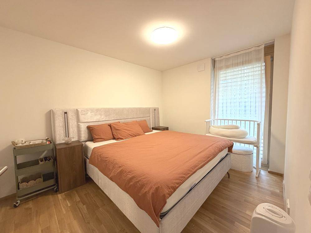 Helles Schlafzimmer mit Doppelbett, Holzboden und Fenster mit Rollladen.