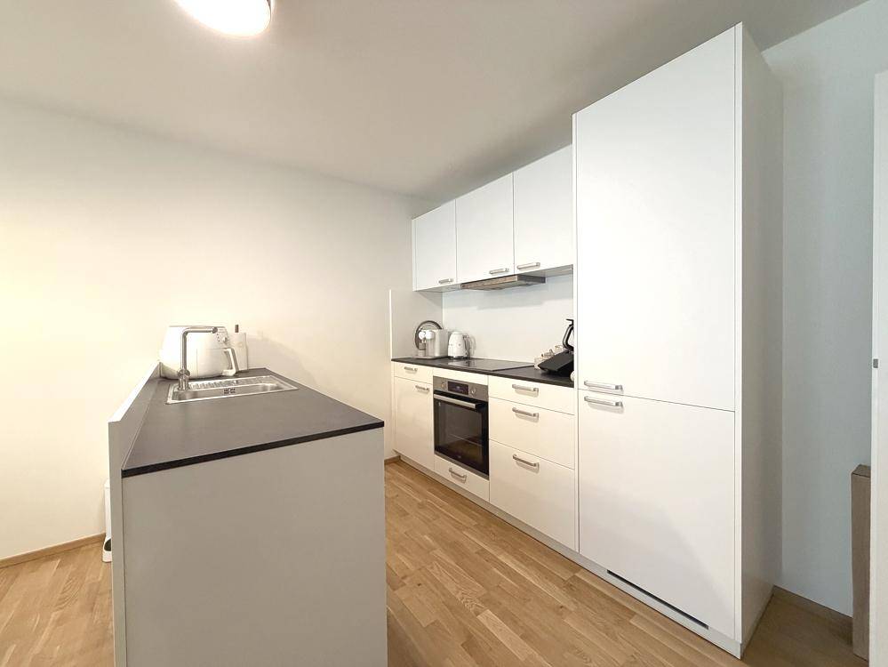 Moderne weiße Küche mit dunkler Arbeitsplatte und integrierten Geräten.