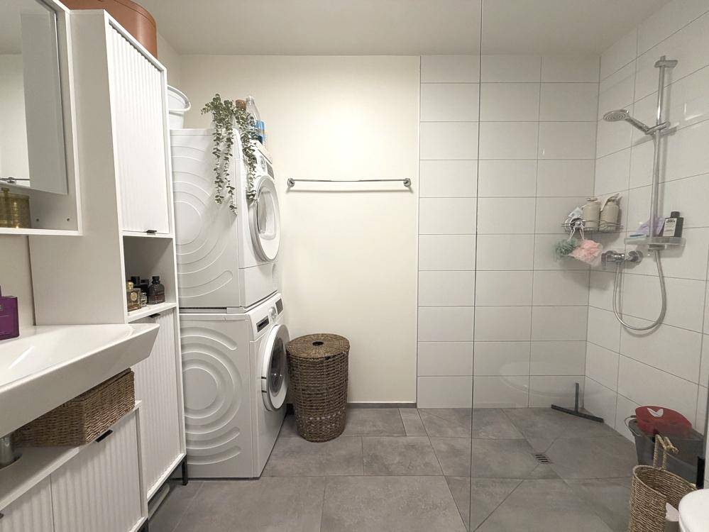 Modernes Badezimmer mit großer Dusche, Waschmaschine und Trockner.