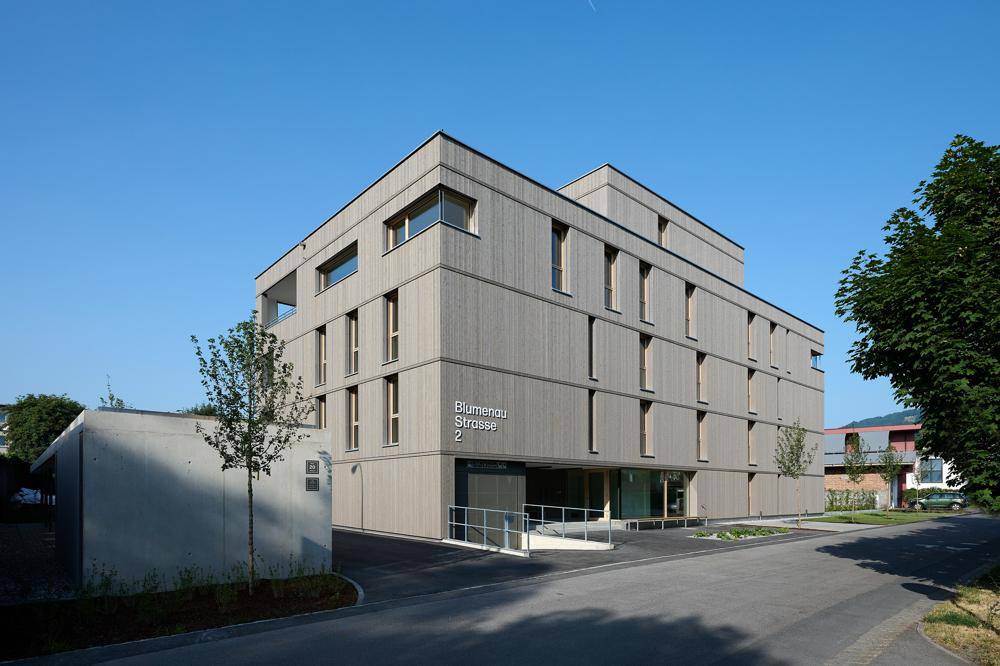 Modernes Mehrfamilienhaus mit Holzfassade und barrierefreiem Zugang.