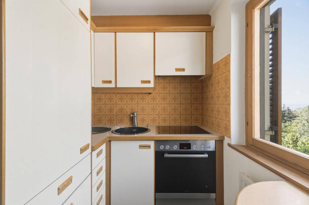 Kleine Küche mit weißen Schränken, Holzdetails und einem Fenster mit Blick ins Grüne.
