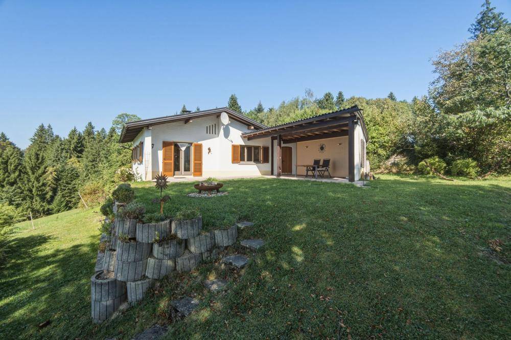 Freistehendes Haus mit großem Garten, überdachter Terrasse und terrassierten Beeten.