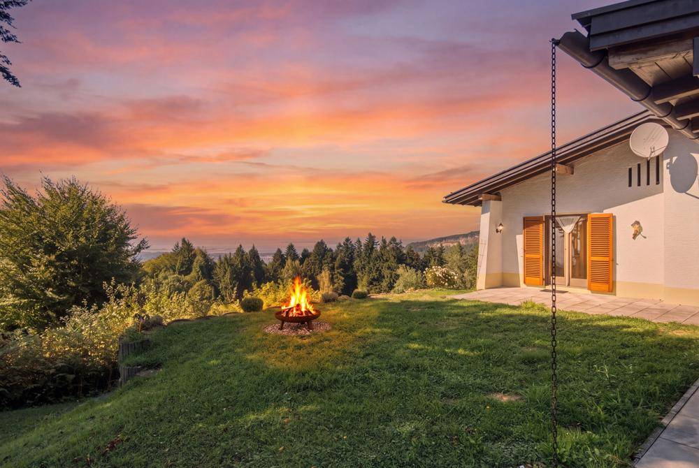Garten mit Feuerstelle und Terrasse bei Sonnenuntergang, mit weitem Blick auf die Landschaft.