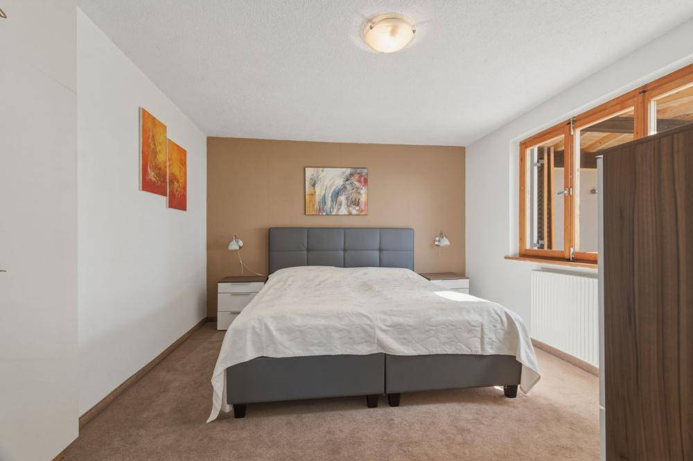 Gemütliches Schlafzimmer mit Doppelbett, Teppichboden und einem Fenster mit Holzrahmen.