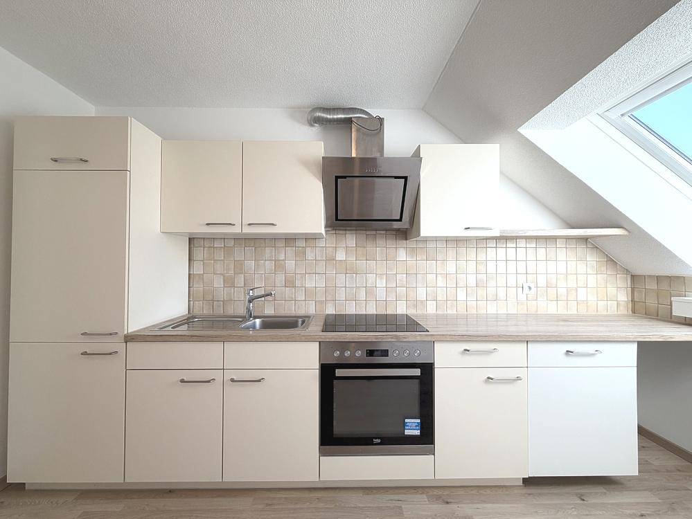 Funktionale Einbauküche mit hellen Schränken, Induktionskochfeld und Dachfenster, gut ausgestattet.