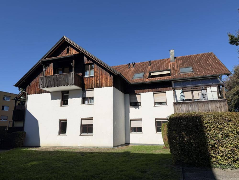 Ansicht des Gebäudes mit weißer Fassade, Holzelementen und Satteldach, umgeben von Grünflächen.