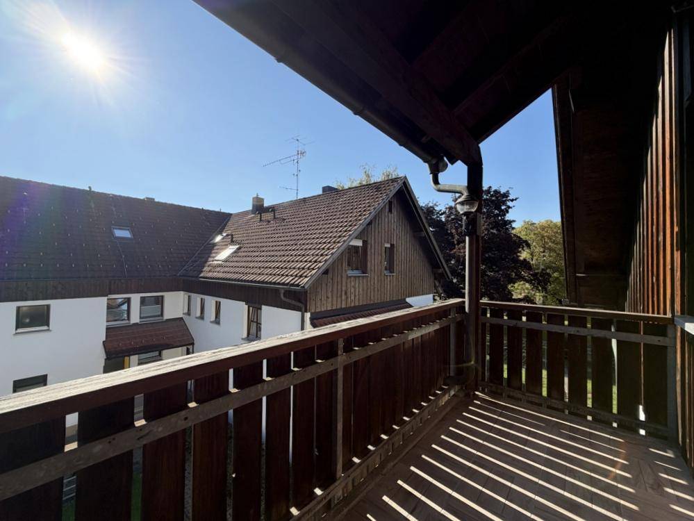 Sonniger Holzbalkon mit Blick auf die umliegenden Häuser und viel Grün.