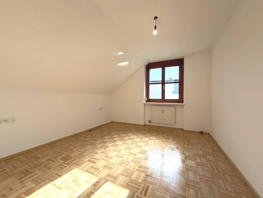 Geräumiges Zimmer mit Dachschräge, Holzfenster und Parkettboden, bietet vielseitige Nutzungsmöglichkeiten.