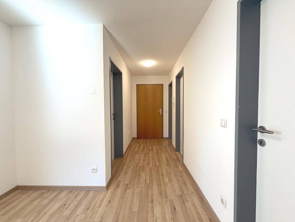 Heller Flur mit mehreren Türen und durchgehendem Laminatboden, der zu den Zimmern führt.
