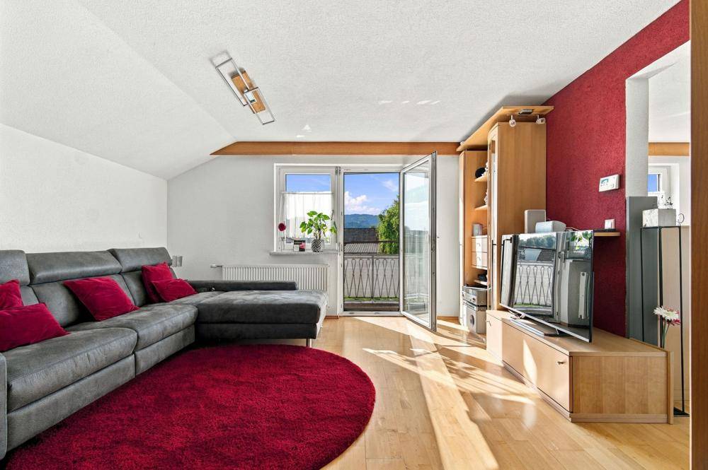 Helles Wohnzimmer mit rotem Teppich, bequemer Couch und Zugang zum Balkon.