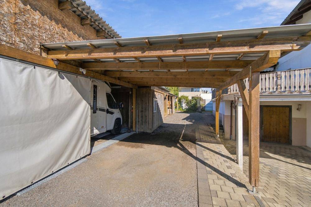 Überdachter Carport mit Holzbalken und Stellplatz für Fahrzeuge.