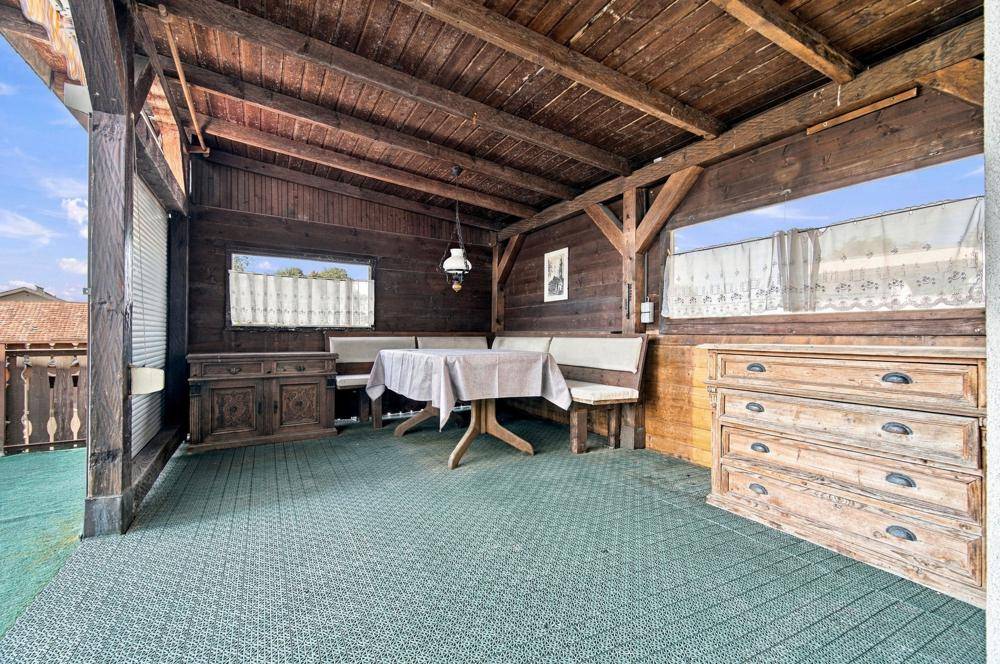 Überdachter Holzbalkon mit rustikalem Essbereich und Blick ins Grüne.