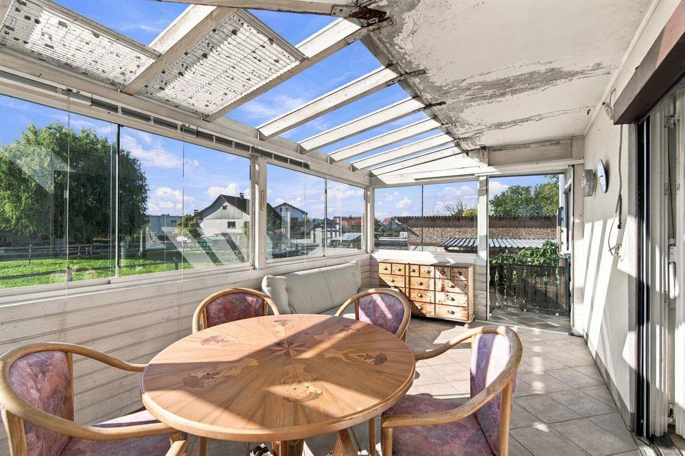 Verglaster Wintergarten mit Esstisch und Blick auf die Umgebung.