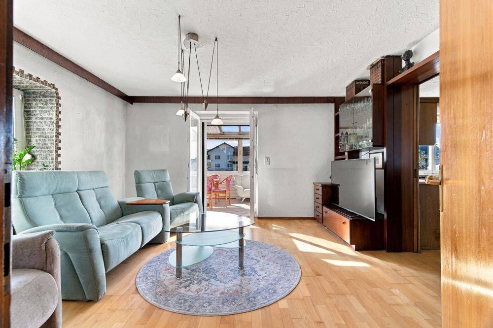Wohnzimmer mit hellblauer Couch, Holzbalken und Zugang zu einem verglasten Balkon.