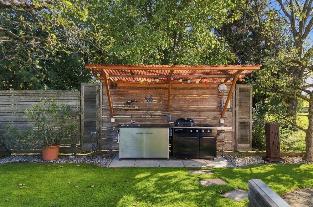Gartenbereich mit Grillstation, Rasenfläche und hohen Bäumen.