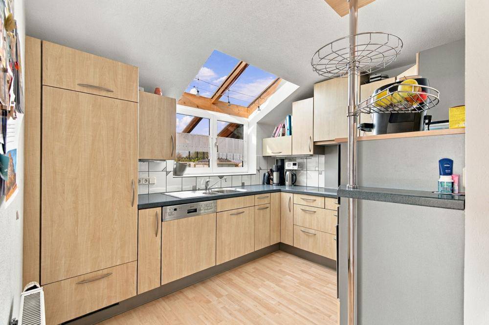 Funktionale Küche mit hellen Holzfronten, Dachfenster und integrierten Geräten.