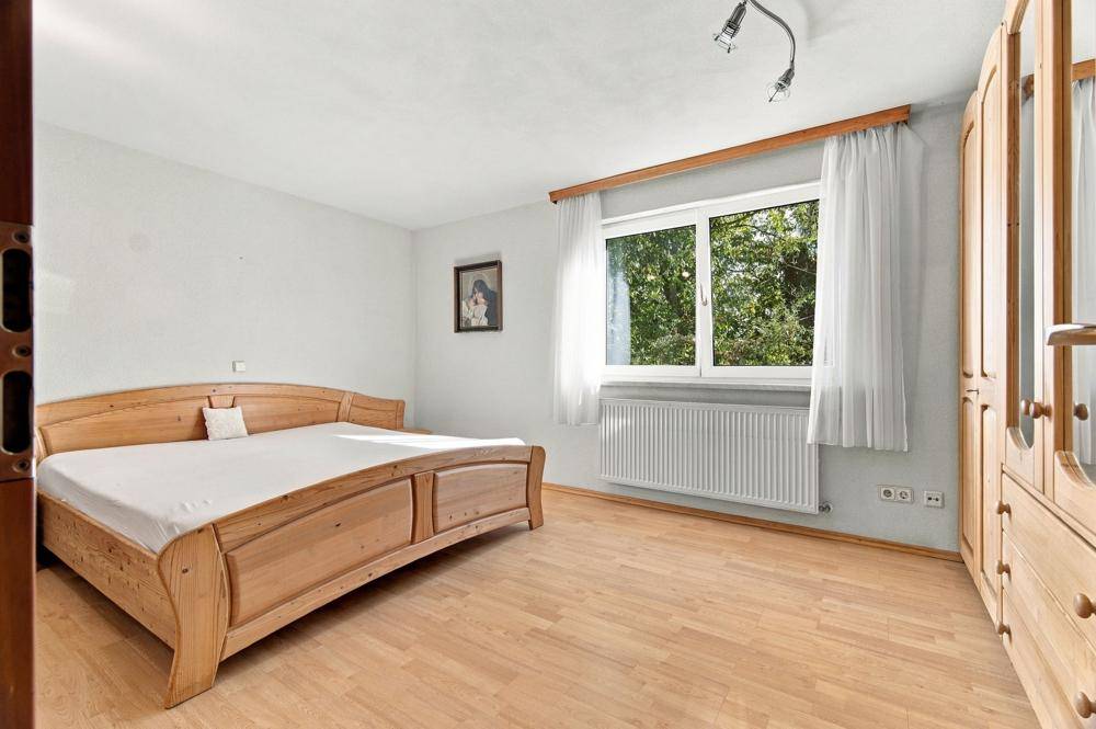 Helles Schlafzimmer mit Holzdoppelbett, Parkettboden und Blick ins Grüne.