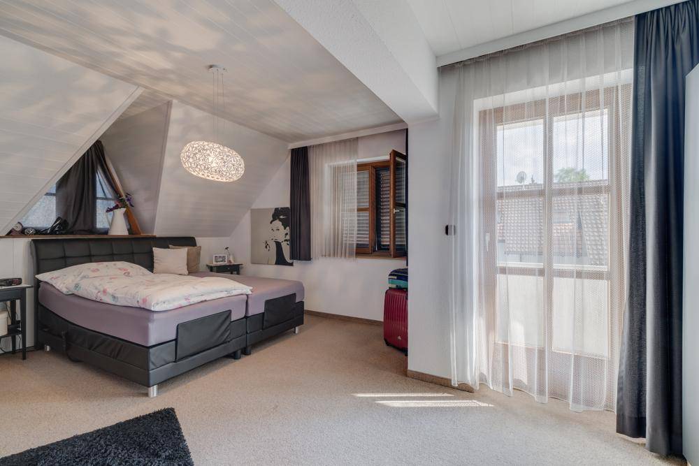 Schlafzimmer im Dachgeschoss mit Teppichboden, Dachschräge und großem Fenster für viel Licht.