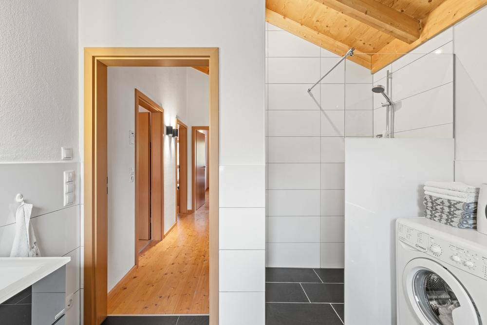 Modernes Badezimmer mit begehbarer Dusche, Waschmaschine und Holzdachschräge.