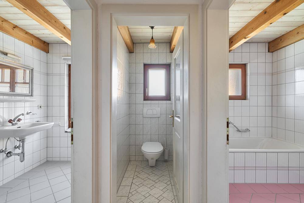 Badezimmer mit Badewanne und separatem WC, beide mit Fliesen und Holzdecken.