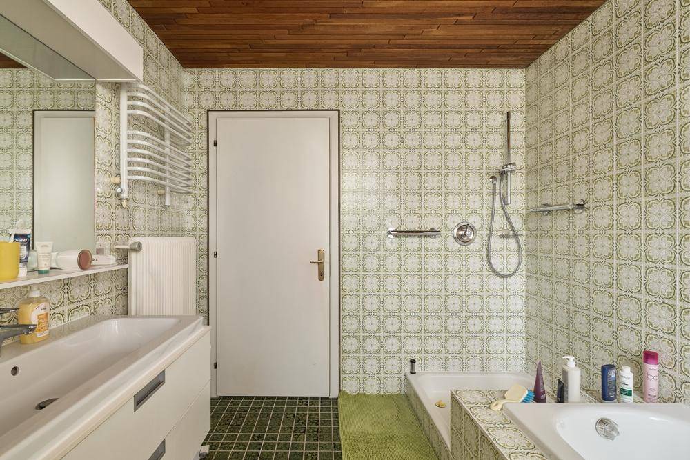 Badezimmer im Retro-Stil mit grünen Fliesen, Badewanne und Holzdecke.