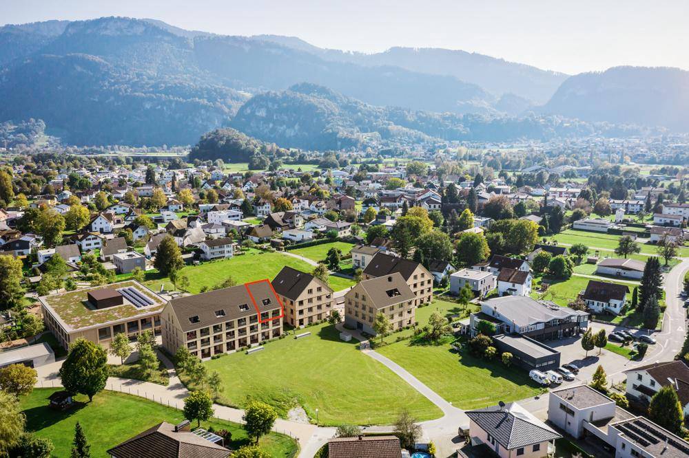Luftaufnahme einer Wohnsiedlung mit mehreren Gebäuden und Bergblick in ländlicher Umgebung.