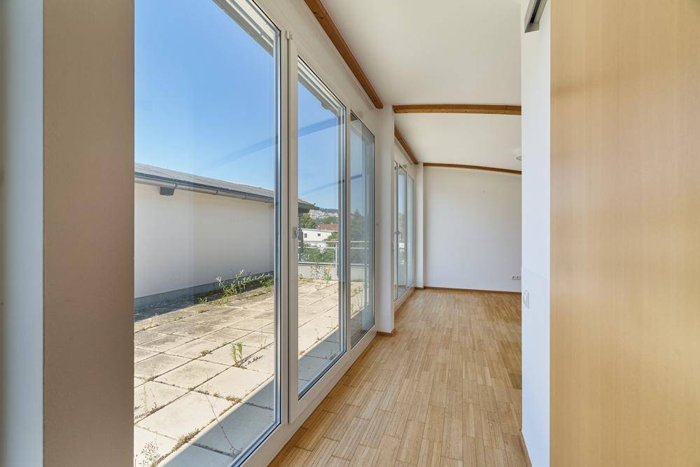 Heller Flur mit Holzboden und großen Fenstern, die auf eine Terrasse blicken.