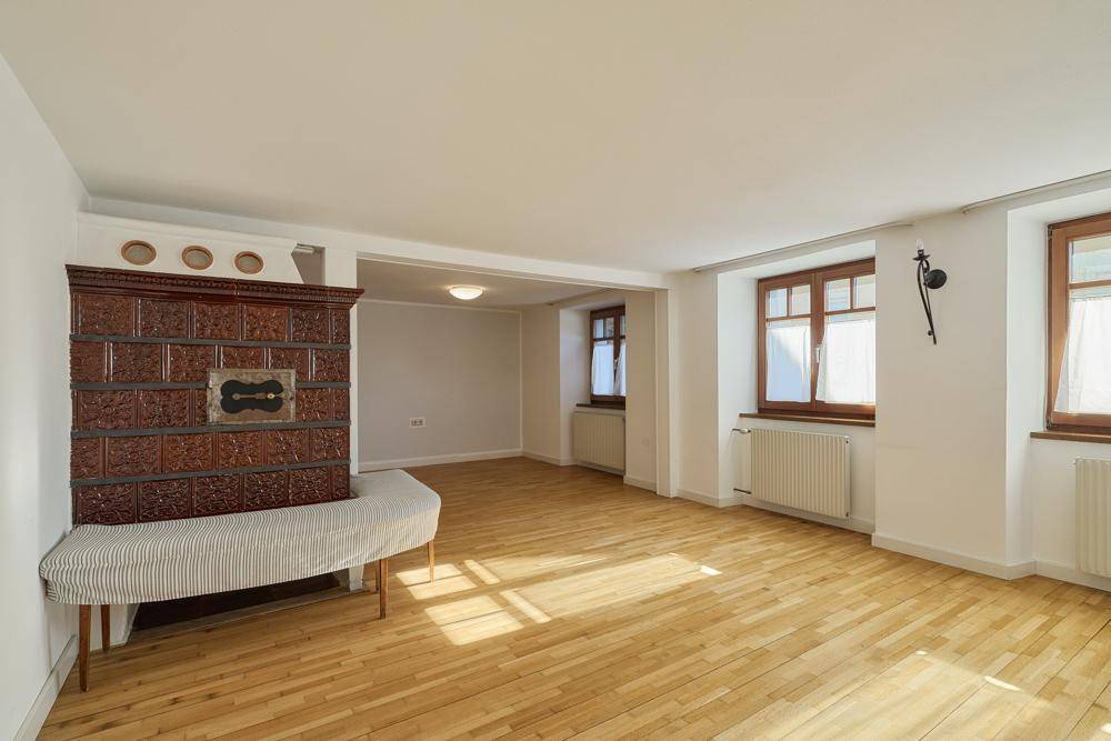 Geräumiges Wohnzimmer mit traditionellem Kachelofen und hellem Holzparkettboden.