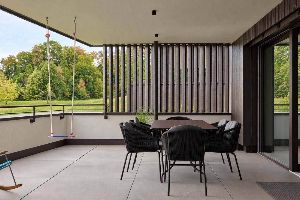 Großer Balkon mit Esstisch, Schaukel und Blick auf die umliegende Natur.
