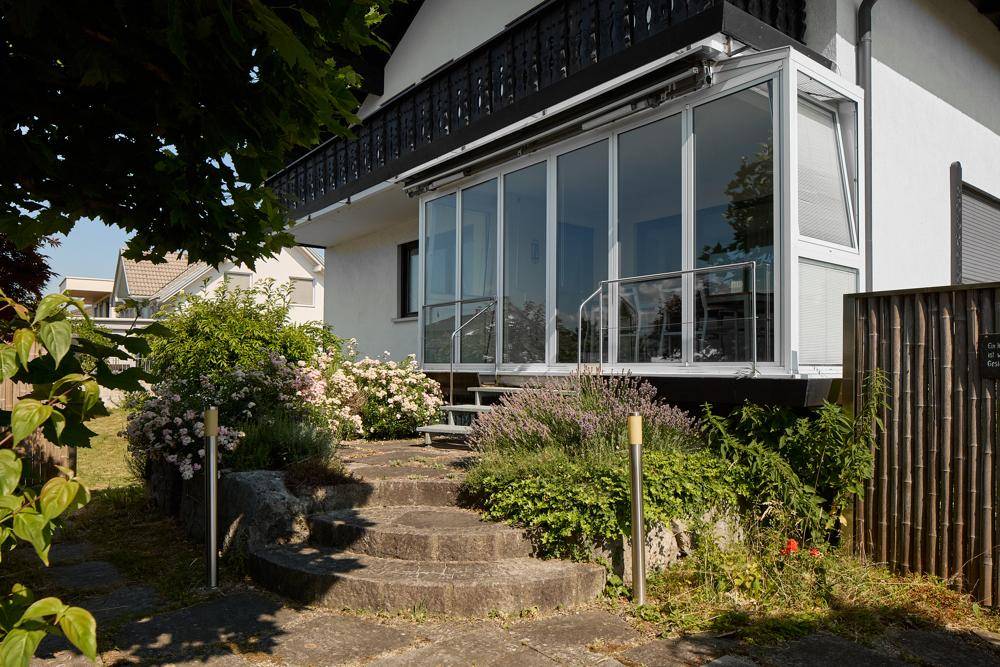 Verglaster Wintergarten mit Zugang zum Garten und Steintreppe umgeben von Pflanzen.