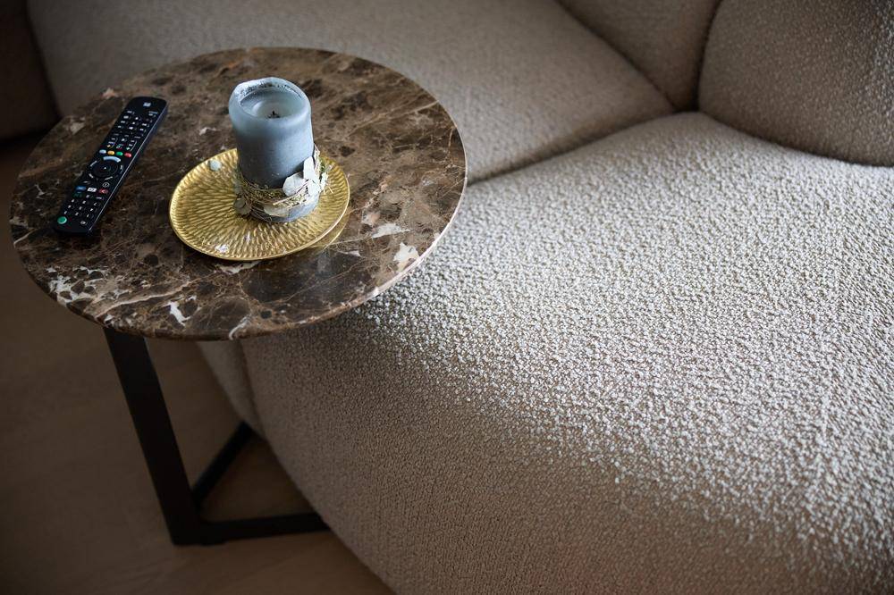 Detailaufnahme eines modernen Beistelltisches mit Marmorplatte neben einem bequemen Sofa.