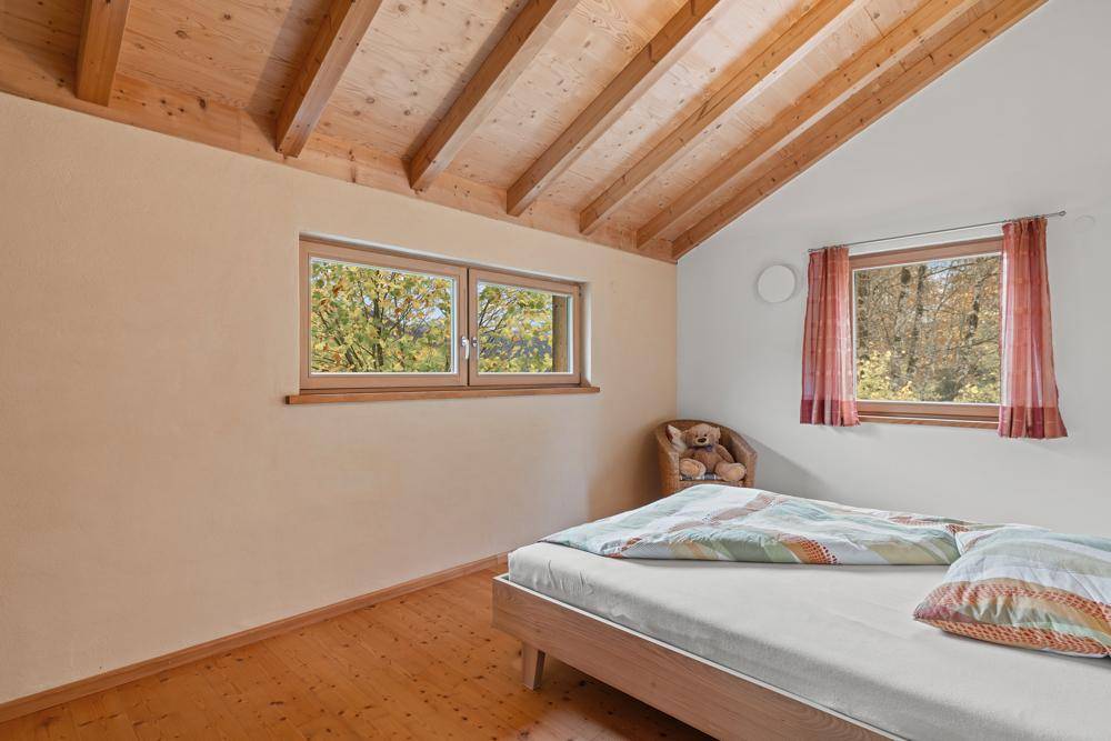 Gemütliches Schlafzimmer mit Holzdachschräge, Doppelbett und Fenstern mit Blick ins Grüne.
