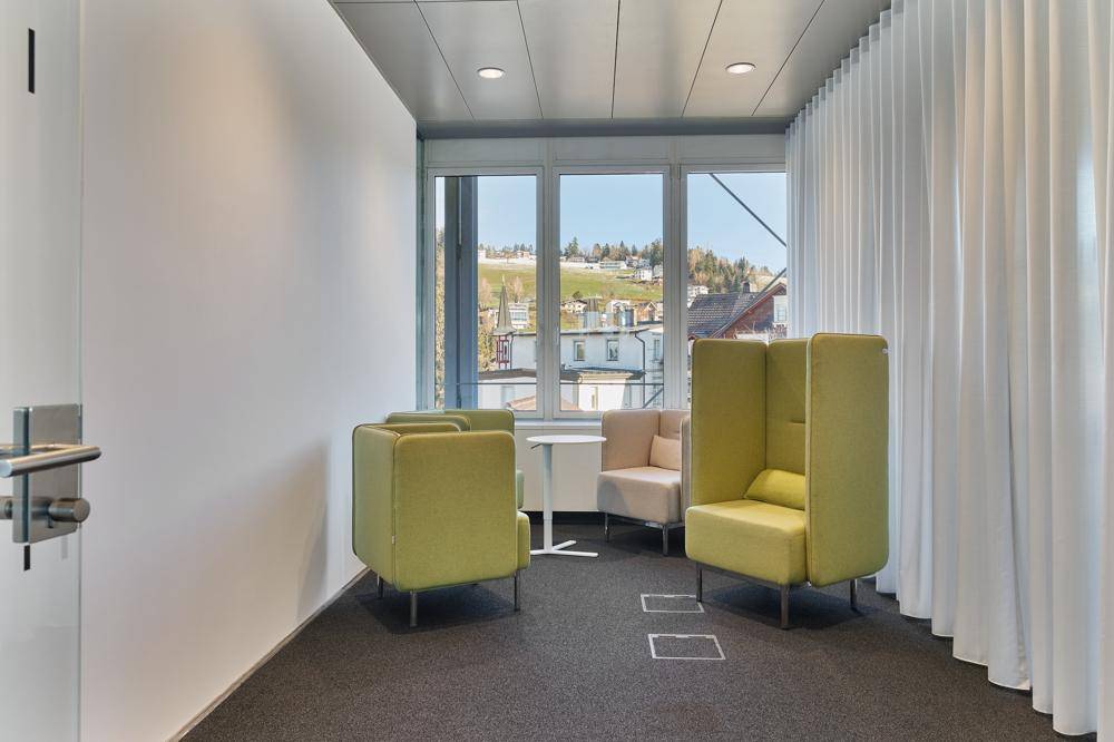 Gemütlicher Besprechungsbereich mit modernen Sesseln, kleinem Tisch und Blick auf die hügelige Landschaft.