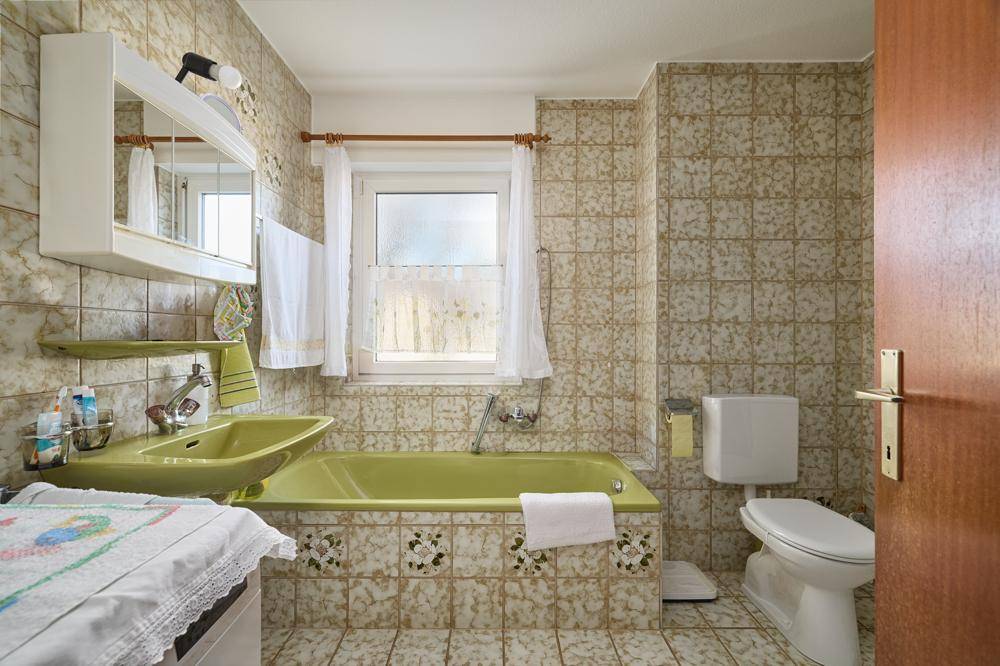 Badezimmer im Stil der 80er Jahre mit grüner Badewanne, Waschbecken und gemusterten Fliesen.