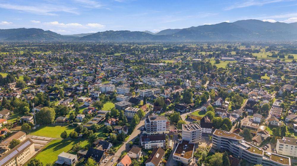 Panoramische Luftaufnahme einer Siedlung mit grünen Flächen und majestätischen Bergen am Horizont.
