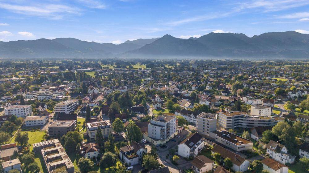 Weitläufige Luftaufnahme einer Stadt oder Gemeinde mit einer beeindruckenden Bergkulisse im Hintergrund.