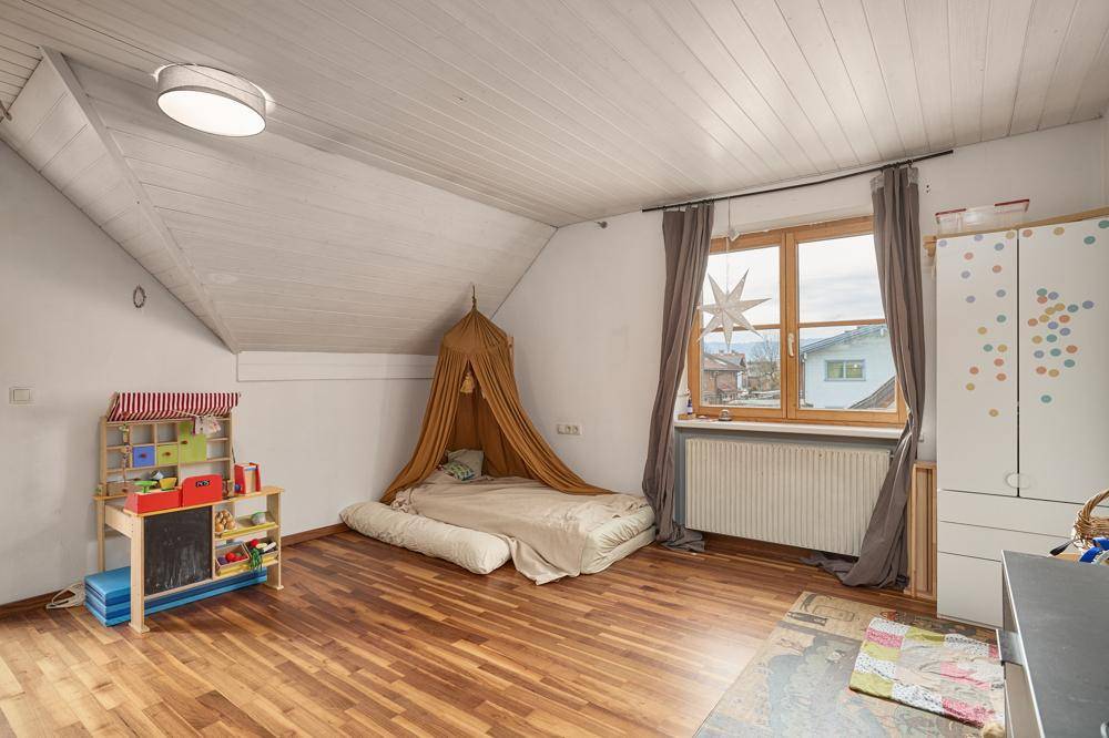 Kinderzimmer mit Holzboden, Dachschräge und hellem Fensterbereich.