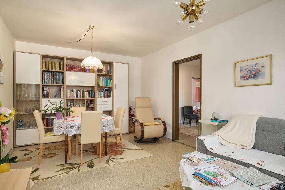 Kombinierter Wohn- und Essbereich mit Esstisch, Sofa und Bücherregal in heller Atmosphäre.