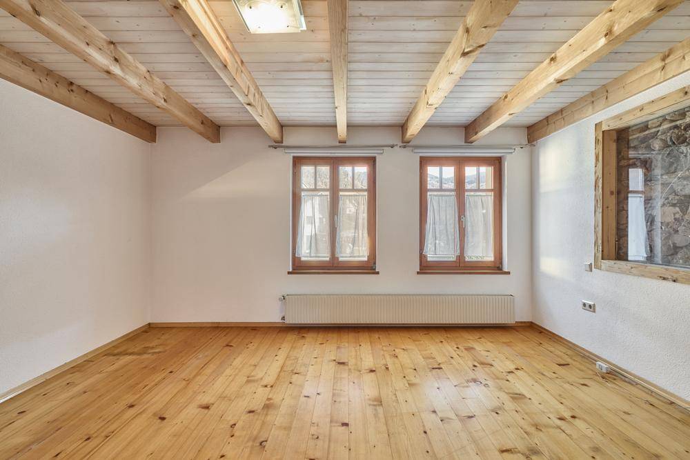 Helles Schlafzimmer mit Holzbalkendecke, Holzfußboden und zwei Fenstern.