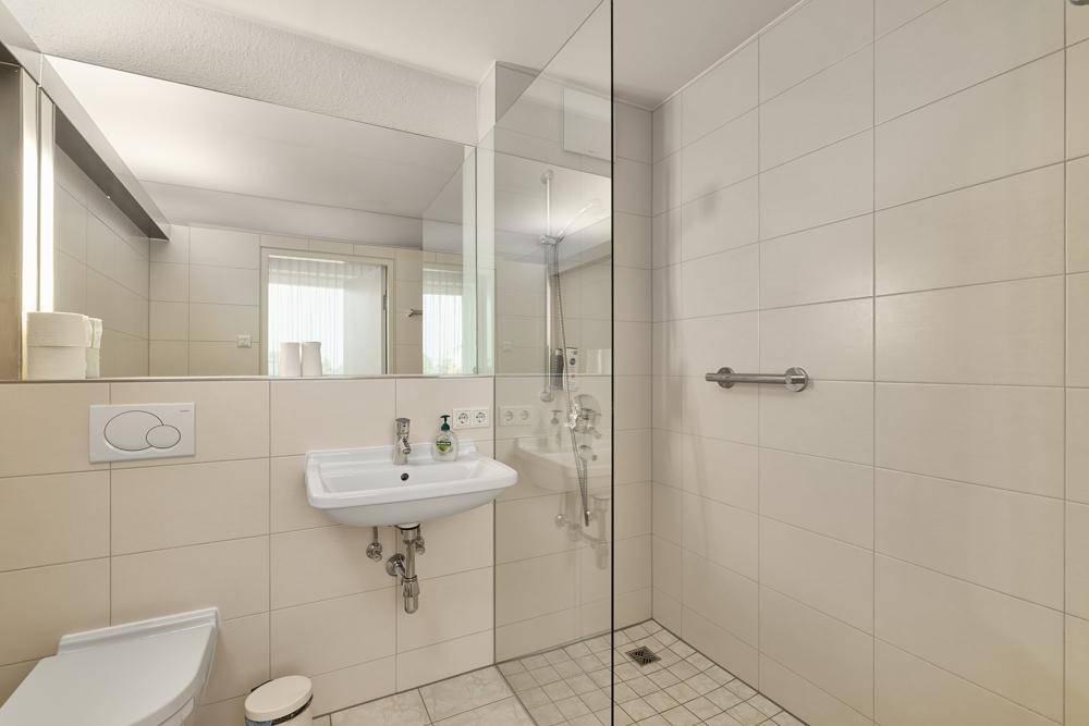 Modernes Badezimmer mit begehbarer Dusche, Einzelwaschbecken und hellen Fliesen.