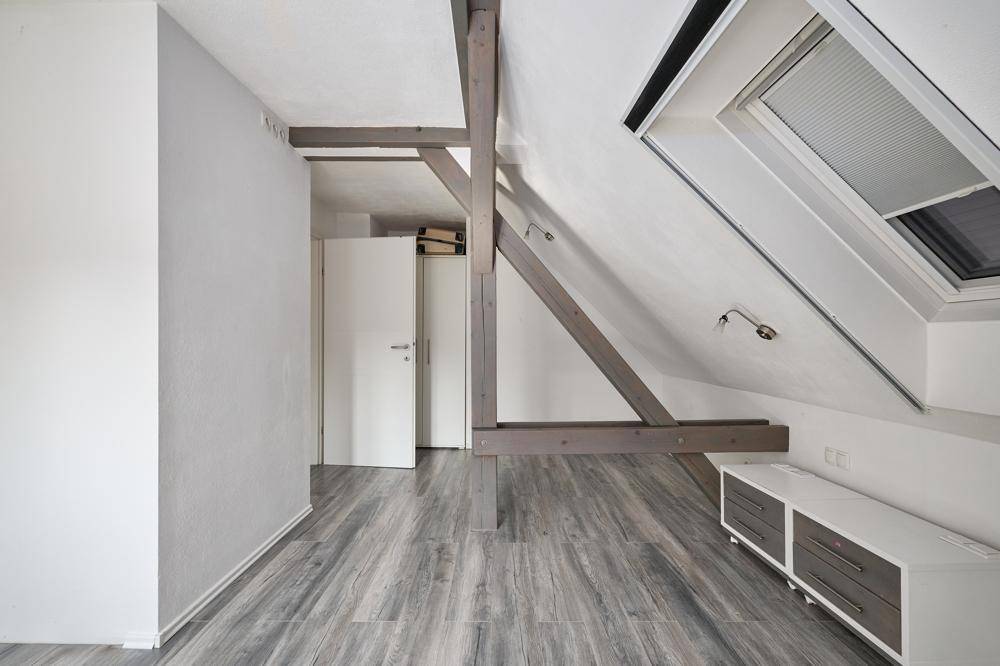 Helles Dachzimmer mit sichtbaren Holzbalken, schräger Decke und einem Dachfenster.