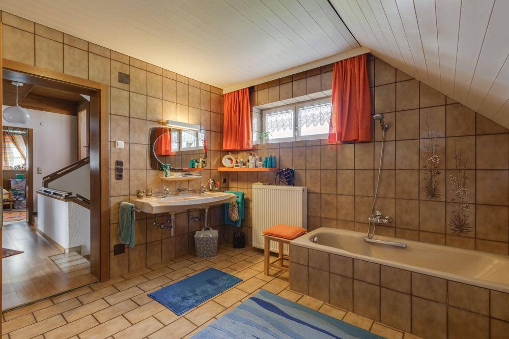 Geräumiges Badezimmer im 80er-Jahre-Stil mit Badewanne, braunen Fliesen und Dachschräge.