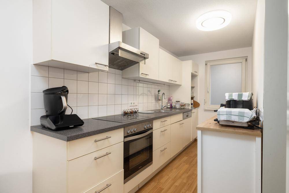 Funktionale Küche mit weißen Schränken, dunkler Arbeitsplatte und modernen Geräten.