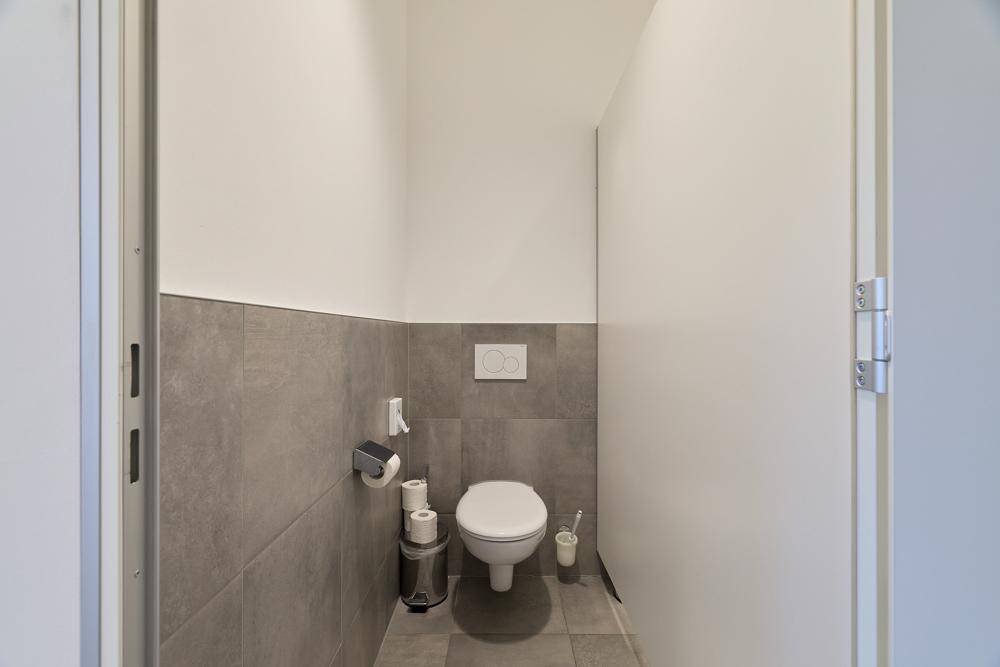 Saubere Toilette mit Wand-WC, grauen Fliesen und minimalistischer Gestaltung.
