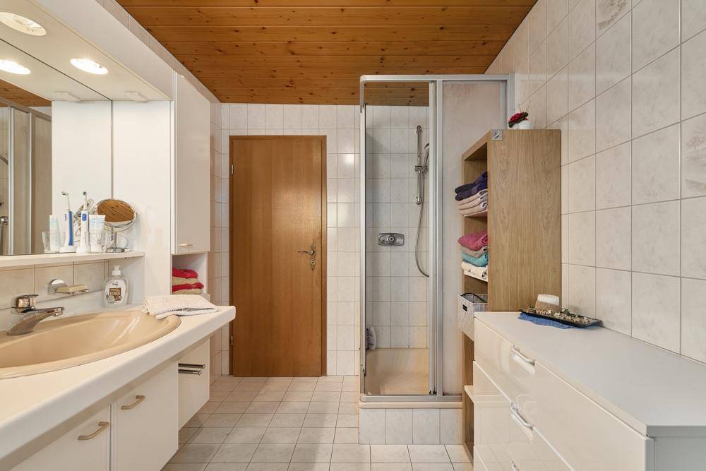 Gefliestes Badezimmer mit Dusche, Einzelwaschbecken und Holzdecke.