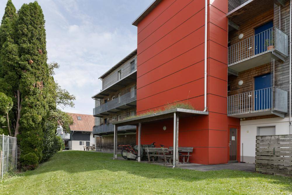 Gepflegte Grünfläche neben dem Gebäude mit roter Fassade und Balkonen.