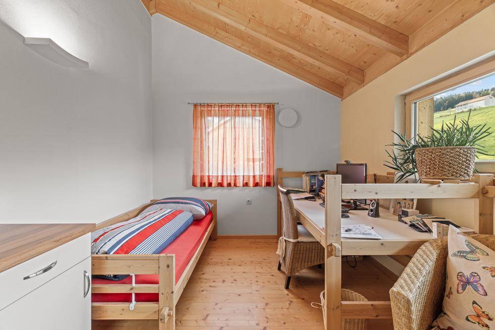 Helles Schlafzimmer mit Holzdachschräge, Einzelbett und Schreibtisch am Fenster.