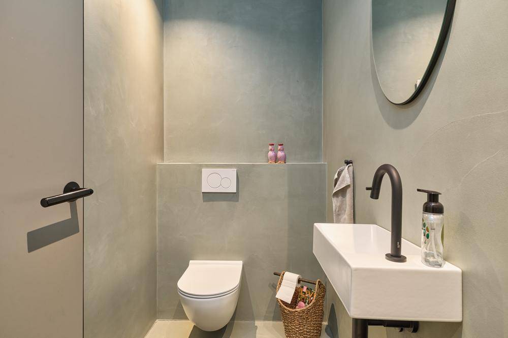 Stilvolles Gäste-WC mit Wand-WC, modernem Waschbecken und rundem Spiegel.